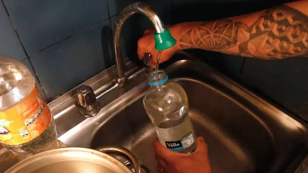 Persona llenando una botella con agua en una cocina