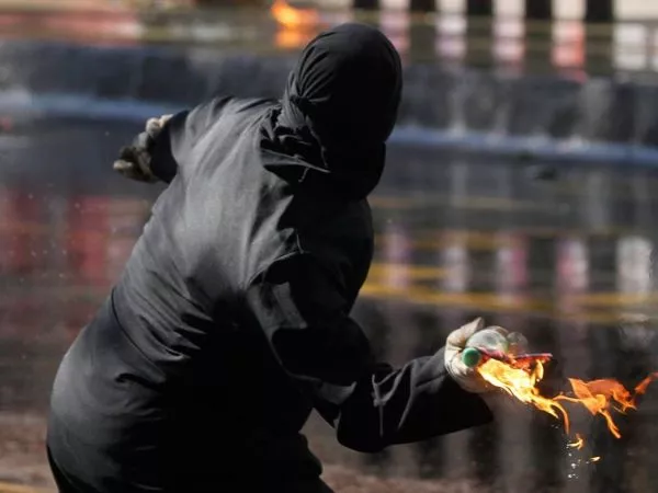 Encapuchado lanzando una bomba molotov