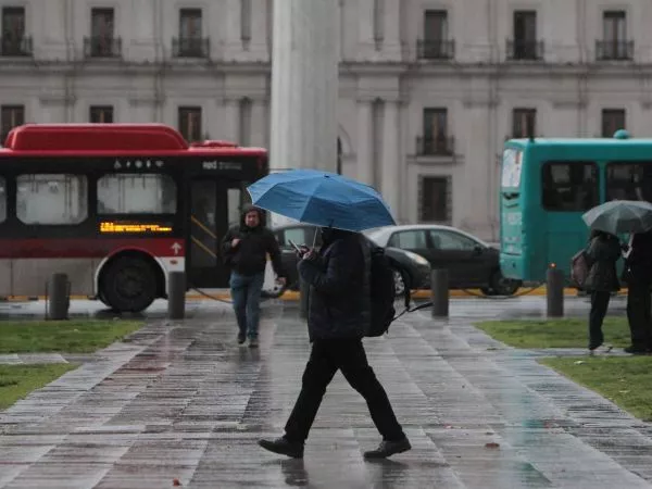 Persona caminando con un paraguas bajo la lluvia frente al Palacio de La Moneda