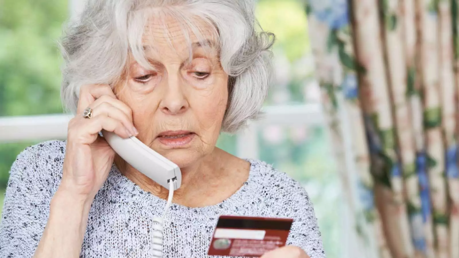 Adulta mayor en el teléfono leyendo los datos de su tarjeta de crédito