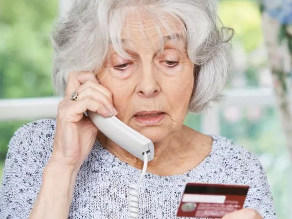 Adulta mayor en el teléfono leyendo los datos de su tarjeta de crédito