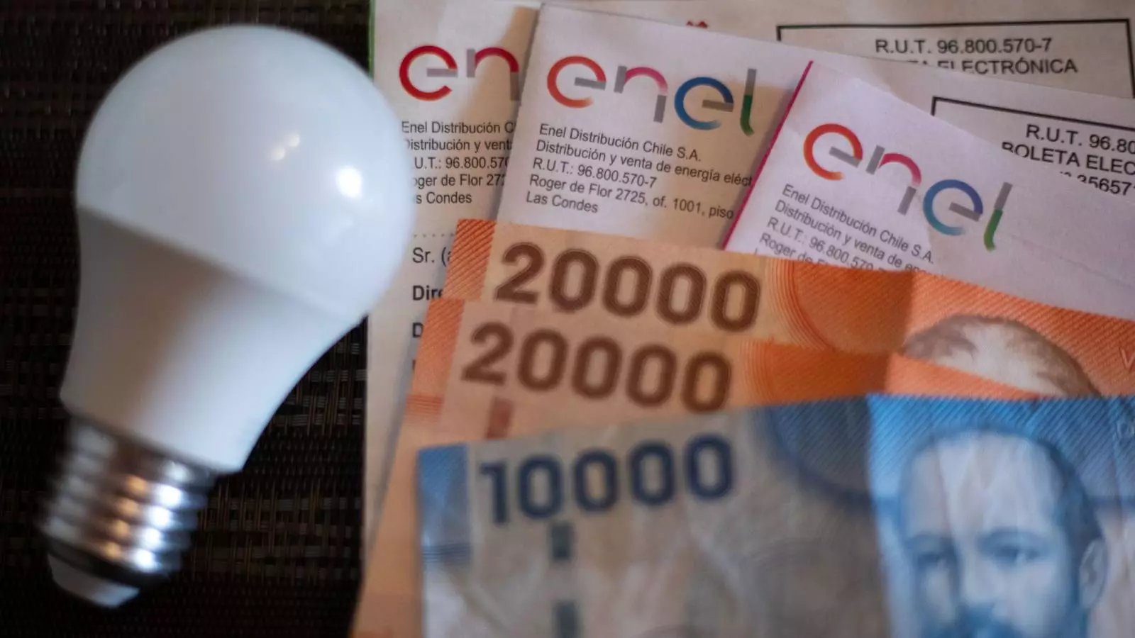 Ampolleta apagada, billetes de distinta denominación y varias boletas de cuentas de la luz de Enel